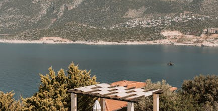 A luxurious villa patio with a pool and sun loungers overlooks a calm blue sea and a mountain landscape.