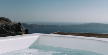 A bubbling hot tub with a view of the sea and distant cliffs under a clear blue sky.